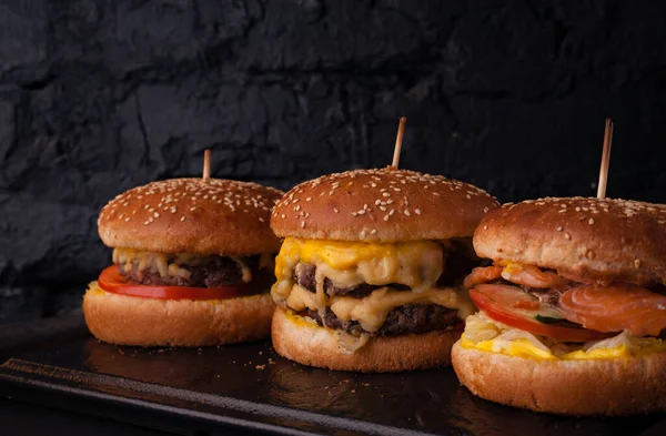 Siyah tuğlalı arka planda arka arkaya çeşitli hamburgerler. Hamburger, çizburger, balık burger..