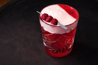 Kırmızı, köpüklü böğürtlen kokteyli. Bardakta ahududu ile süslenmiş..