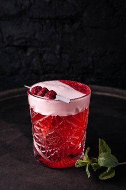 Kırmızı, köpüklü böğürtlen kokteyli. Bardakta ahududu ile süslenmiş..