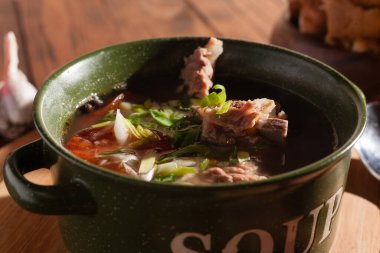 Köy eti çorbası / çorba üzerine yeşil soğan serpiştirilmiş ahşap bir masada kraker.