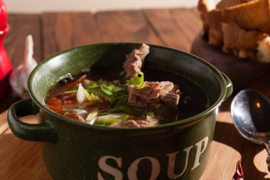 Köy eti çorbası / çorba üzerine yeşil soğan serpiştirilmiş ahşap bir masada kraker.