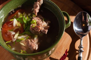 Köy eti çorbası / çorba üzerine yeşil soğan serpiştirilmiş ahşap bir masada kraker.