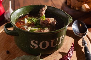 Köy eti çorbası / çorba üzerine yeşil soğan serpiştirilmiş ahşap bir masada kraker.