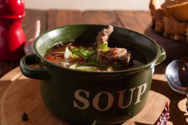 Köy eti çorbası / çorba üzerine yeşil soğan serpiştirilmiş ahşap bir masada kraker.