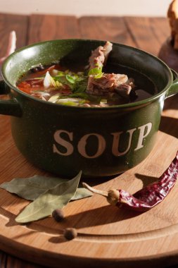 Köy eti çorbası / çorba üzerine yeşil soğan serpiştirilmiş ahşap bir masada kraker.