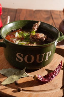 Köy eti çorbası / çorba üzerine yeşil soğan serpiştirilmiş ahşap bir masada kraker.