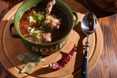 Köy eti çorbası / çorba üzerine yeşil soğan serpiştirilmiş ahşap bir masada kraker.