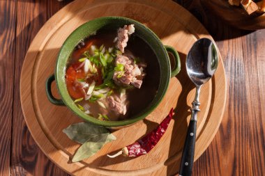 Köy eti çorbası / çorba üzerine yeşil soğan serpiştirilmiş ahşap bir masada kraker.
