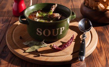 Köy eti çorbası / çorba üzerine yeşil soğan serpiştirilmiş ahşap bir masada kraker.