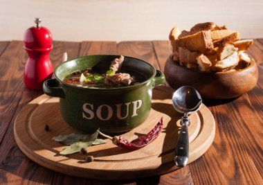 Köy eti çorbası / çorba üzerine yeşil soğan serpiştirilmiş ahşap bir masada kraker.