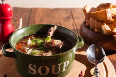 Köy eti çorbası / çorba üzerine yeşil soğan serpiştirilmiş ahşap bir masada kraker.