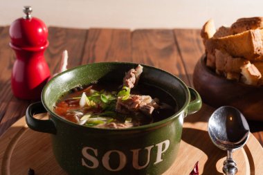 Köy eti çorbası / çorba üzerine yeşil soğan serpiştirilmiş ahşap bir masada kraker.