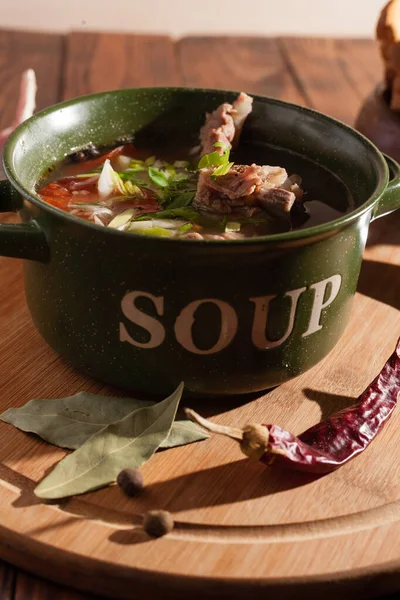 Köy eti çorbası / çorba üzerine yeşil soğan serpiştirilmiş ahşap bir masada kraker.