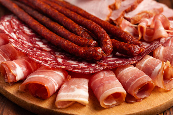 Assorted meat snacks on a wooden cutting board. Sausage, ham, bacon, smoked meats. Stock photo of meat products with blank space.
