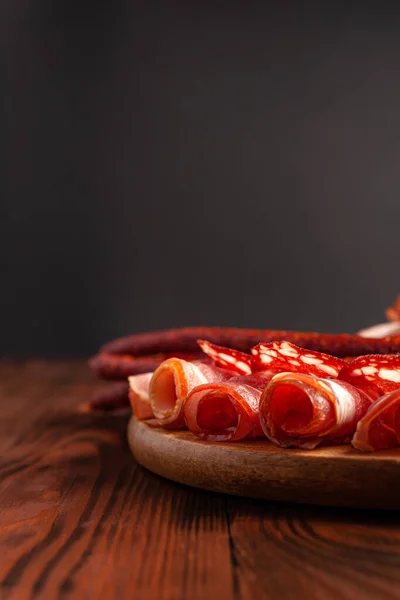 Assorted meat snacks on a wooden cutting board. Sausage, ham, bacon, smoked meats. Stock photo of meat products with blank space.