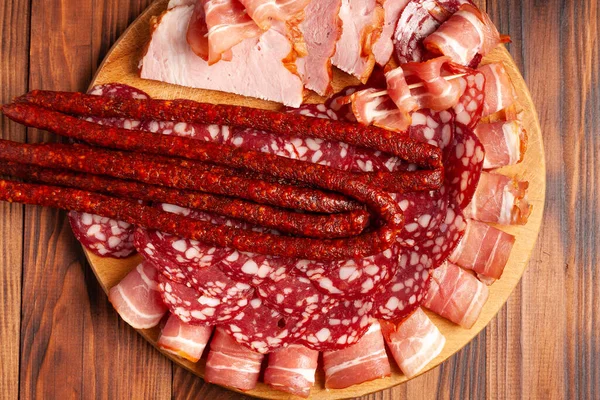 Assorted meat snacks on a wooden cutting board. Sausage, ham, bacon, smoked meats. Stock photo of meat products with blank space.
