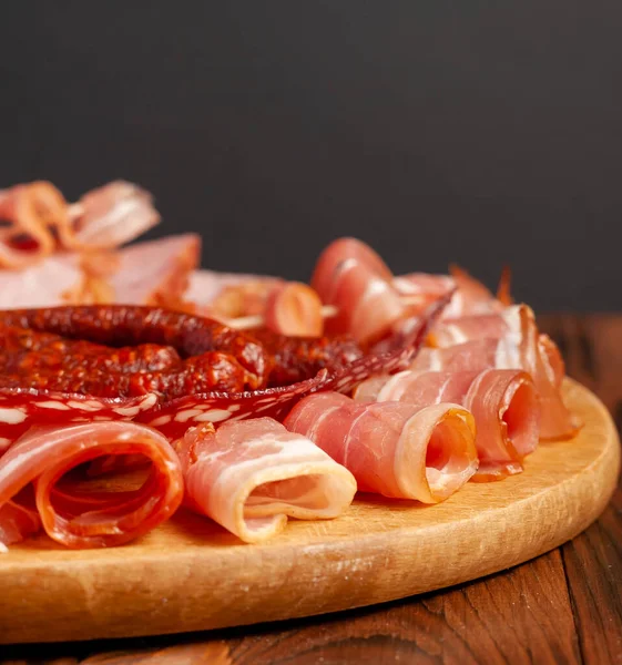 Assorted meat snacks on a wooden cutting board. Sausage, ham, bacon, smoked meats. Stock photo of meat products with blank space.