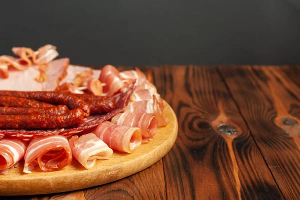 Assorted meat snacks on a wooden cutting board. Sausage, ham, bacon, smoked meats. Stock photo of meat products with blank space.