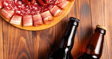 Et ürünleri ve şişe bira şeklinde atıştırmalıklar. Pastırma, salam, jambon ve av sosisi şeklinde aperatif. Stok fotoğraf birası ve ahşap bir masada atıştırmalık.