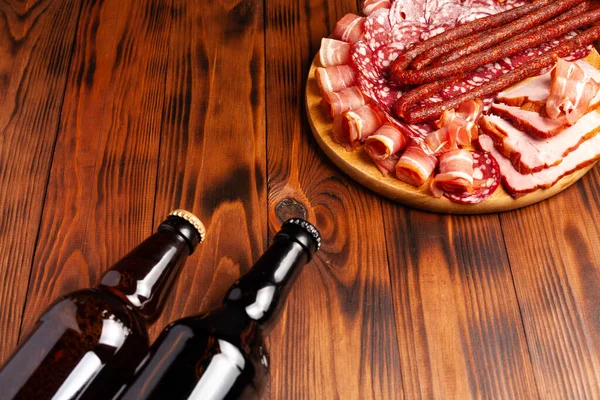 Beer snack in the form of meat products and bottled beer. Appetizer in the form of slicing bacon, salami, ham, hunting sausages. Stock photo beer and snack on a wooden table.