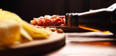 Ahşap arka plandaki her tat için iki şişe bira ve çeşitli atıştırmalıklar. Et ürünleri, sosis dilimleri, cips, fındık, kızarmış ekmek..