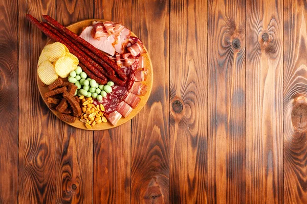 Assorted beer snacks on a wooden table with copy space. Sausage, ham, bacon. Salty snack chips, croutons, peanuts, wasabi nuts. — Stock Image Assorted Beer Snacks Wooden Table Copy Space Sausage Ham Bacon Royalty Free Stock Images