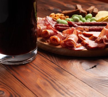 Bir kupa bira ve ahşap bir masada çeşitli atıştırmalıklar. Sosis, salam, jambon, pastırma. Bira, tuzlu çerez, cips, wasabi fındığı, tuzlu fıstık, kızarmış ekmek..