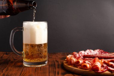 Bir kupa bira ve ahşap bir masada çeşitli atıştırmalıklar. Sosis, salam, jambon, pastırma. Bira, tuzlu çerez, cips, wasabi fındığı, tuzlu fıstık, kızarmış ekmek..