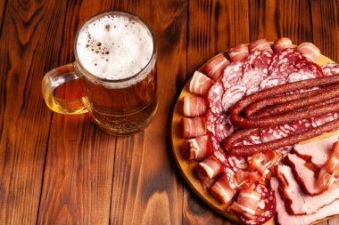 Bir kupa bira ve ahşap bir masada çeşitli atıştırmalıklar. Sosis, salam, jambon, pastırma. Bira, tuzlu çerez, cips, wasabi fındığı, tuzlu fıstık, kızarmış ekmek..