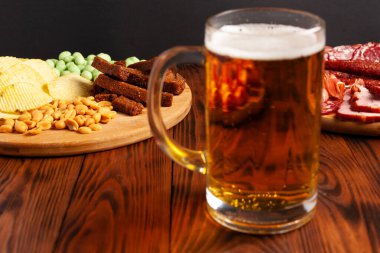 Bir kupa bira ve ahşap bir masada çeşitli atıştırmalıklar. Sosis, salam, jambon, pastırma. Bira, tuzlu çerez, cips, wasabi fındığı, tuzlu fıstık, kızarmış ekmek..