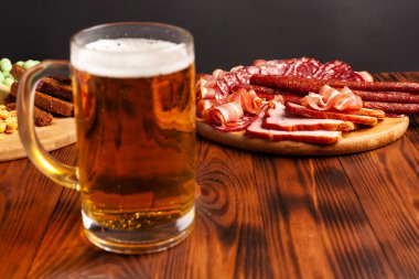 Bir kupa bira ve ahşap bir masada çeşitli atıştırmalıklar. Sosis, salam, jambon, pastırma. Bira, tuzlu çerez, cips, wasabi fındığı, tuzlu fıstık, kızarmış ekmek..