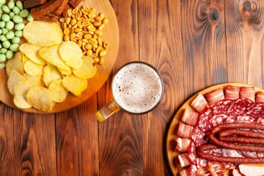 Bir kupa bira ve ahşap bir masada çeşitli atıştırmalıklar. Sosis, salam, jambon, pastırma. Bira, tuzlu çerez, cips, wasabi fındığı, tuzlu fıstık, kızarmış ekmek..