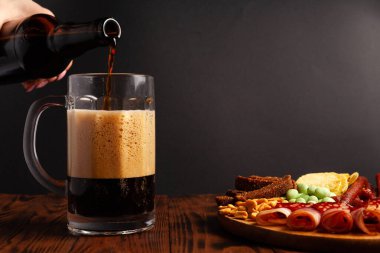 Bir kupa bira ve ahşap bir masada çeşitli atıştırmalıklar. Sosis, salam, jambon, pastırma. Bira, tuzlu çerez, cips, wasabi fındığı, tuzlu fıstık, kızarmış ekmek..