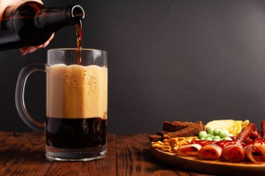 Bir kupa bira ve ahşap bir masada çeşitli atıştırmalıklar. Sosis, salam, jambon, pastırma. Bira, tuzlu çerez, cips, wasabi fındığı, tuzlu fıstık, kızarmış ekmek..