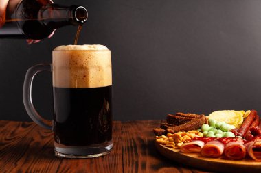 Bir kupa bira ve ahşap bir masada çeşitli atıştırmalıklar. Sosis, salam, jambon, pastırma. Bira, tuzlu çerez, cips, wasabi fındığı, tuzlu fıstık, kızarmış ekmek..