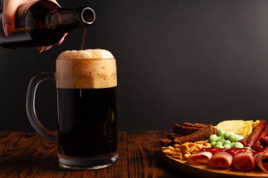 Bir kupa bira ve ahşap bir masada çeşitli atıştırmalıklar. Sosis, salam, jambon, pastırma. Bira, tuzlu çerez, cips, wasabi fındığı, tuzlu fıstık, kızarmış ekmek..