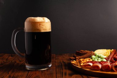 Bir kupa bira ve ahşap bir masada çeşitli atıştırmalıklar. Sosis, salam, jambon, pastırma. Bira, tuzlu çerez, cips, wasabi fındığı, tuzlu fıstık, kızarmış ekmek..