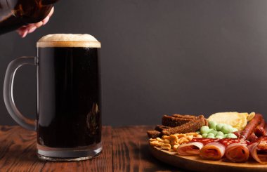 Bir kupa bira ve ahşap bir masada çeşitli atıştırmalıklar. Sosis, salam, jambon, pastırma. Bira, tuzlu çerez, cips, wasabi fındığı, tuzlu fıstık, kızarmış ekmek..