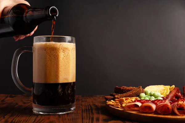 木製のテーブルの上にビールと軽食の品揃えのマグカップ ソーセージ サラミ ベーコン ビールの塩味のスナック チップ わさびナッツ 塩ピーナッツ クルトン — ストック写真