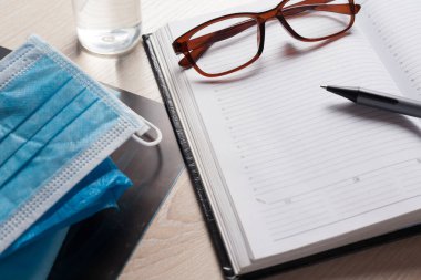 Hastane masasındaki boş not defteri tıbbi ekipmanlarla çevrili. Üst manzara, düz kompozisyon. Not defteri, maske, dezenfektan ve kalem masaya. Virüs 2019-nCoV, koronavirüs, hastalık kavramı. Sağlık kontrolü..