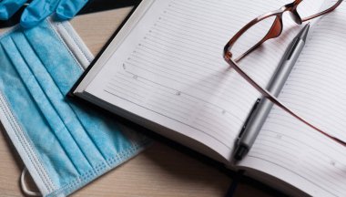 Hastane masasındaki boş not defteri tıbbi ekipmanlarla çevrili. Üst manzara, düz kompozisyon. Not defteri, maske, dezenfektan ve kalem masaya. Virüs 2019-nCoV, koronavirüs, hastalık kavramı. Sağlık kontrolü..