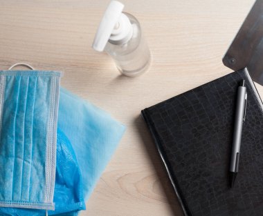 Hastane masasındaki boş not defteri tıbbi ekipmanlarla çevrili. Üst manzara, düz kompozisyon. Not defteri, maske, dezenfektan ve kalem masaya. Virüs 2019-nCoV, koronavirüs, hastalık kavramı. Sağlık kontrolü..