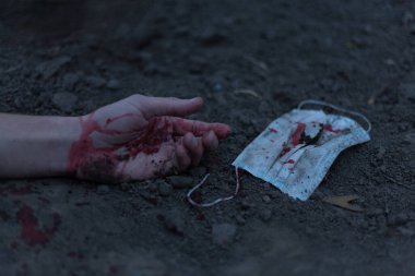 Kanlı bir el uzanıp yerde yatan tıbbi kanlı bir maske. Koronavirüs konsepti ve bu hastalığın neden olduğu kıyamet tüm dünyaya yayıldı. Korkunç..