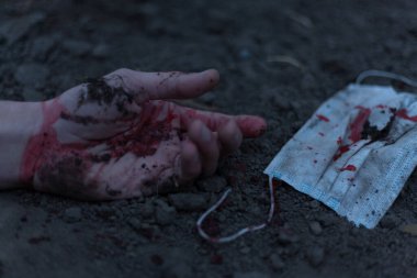 Kanlı bir el uzanıp yerde yatan tıbbi kanlı bir maske. Koronavirüs konsepti ve bu hastalığın neden olduğu kıyamet tüm dünyaya yayıldı. Korkunç..