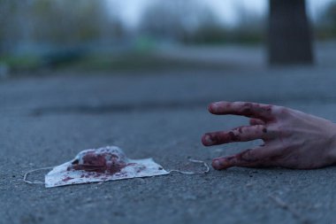 Kanlı bir el uzanıp yerde yatan tıbbi kanlı bir maske. Koronavirüs konsepti ve bu hastalığın neden olduğu kıyamet tüm dünyaya yayıldı. Korkunç..