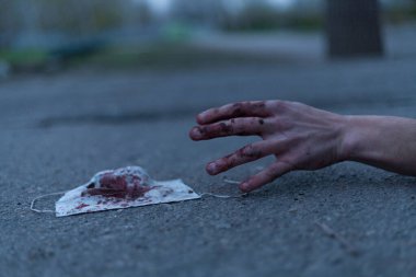 Kanlı bir el uzanıp yerde yatan tıbbi kanlı bir maske. Koronavirüs konsepti ve bu hastalığın neden olduğu kıyamet tüm dünyaya yayıldı. Korkunç..