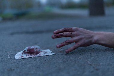 Kanlı bir el uzanıp yerde yatan tıbbi kanlı bir maske. Koronavirüs konsepti ve bu hastalığın neden olduğu kıyamet tüm dünyaya yayıldı. Korkunç..