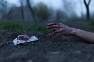 Kanlı bir el uzanıp yerde yatan tıbbi kanlı bir maske. Koronavirüs konsepti ve bu hastalığın neden olduğu kıyamet tüm dünyaya yayıldı. Korkunç..