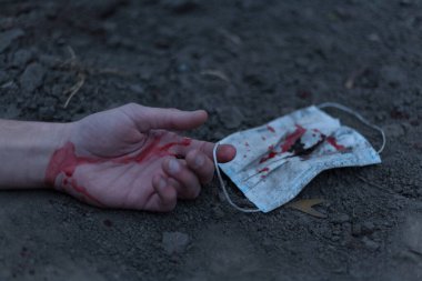 Kanlı bir el uzanıp yerde yatan tıbbi kanlı bir maske. Koronavirüs konsepti ve bu hastalığın neden olduğu kıyamet tüm dünyaya yayıldı. Korkunç..