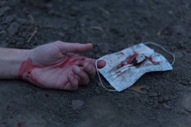 Kanlı bir el uzanıp yerde yatan tıbbi kanlı bir maske. Koronavirüs konsepti ve bu hastalığın neden olduğu kıyamet tüm dünyaya yayıldı. Korkunç..